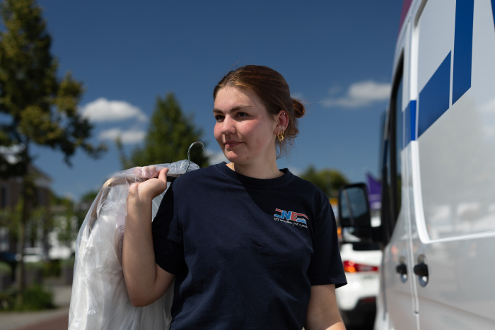 Chauffeuse buiten met hangende goederen over de schouder bij de NE Distriservice bus